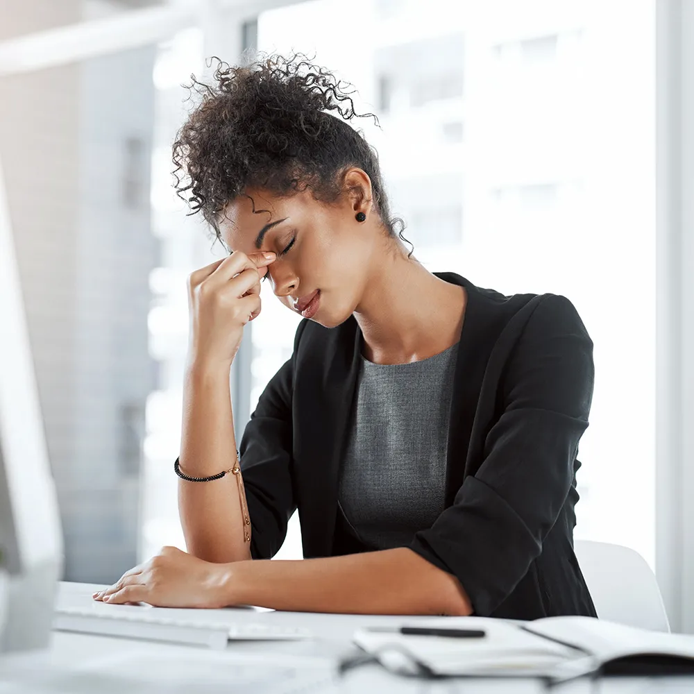 Woman at desk holding nose bridge, migraine