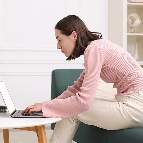 Woman seated, leaning forward while using a laptop.