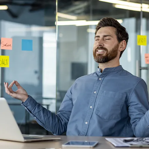 Man in office smiling with closed eyes, sitting in gyan mudra pose.