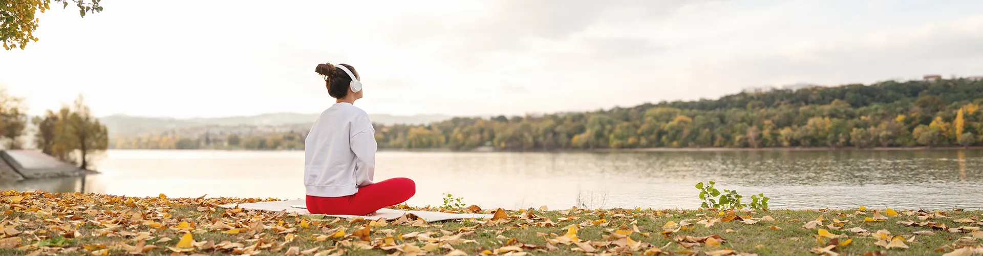 Woman sitting on yoga mat by lake wearing headphones