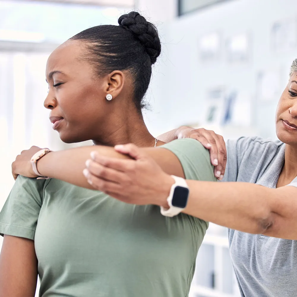 Therapist assisting woman with shoulder stretch.