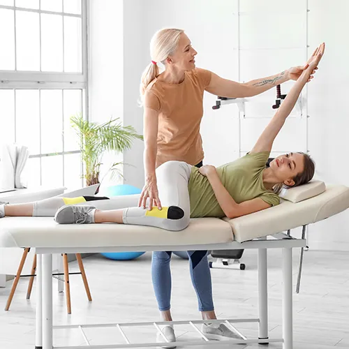 Chiropractor stretching woman’s leg and arm while she lies on her side on therapy bed.