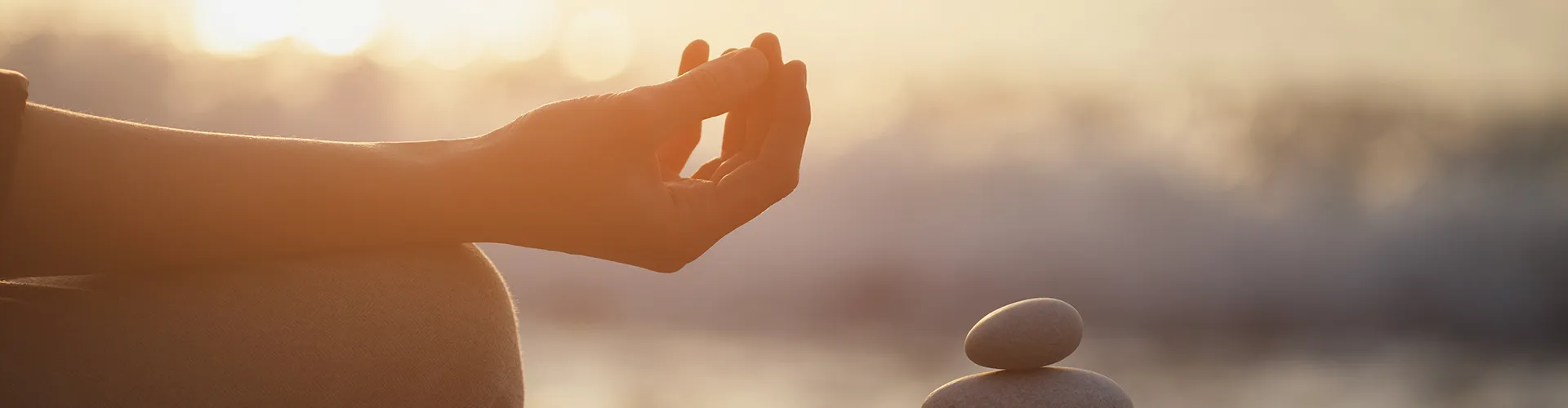 Person sitting in gyan mudra pose next to stacked rocks.