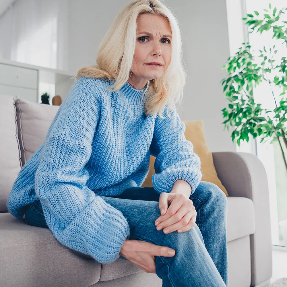 Woman with knee pain on a couch.