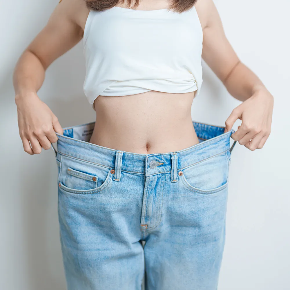 A person showing off weight loss by holding out their oversized jeans.
