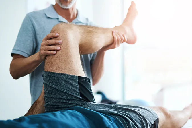 Physical therapist stretching patient’s leg during therapy