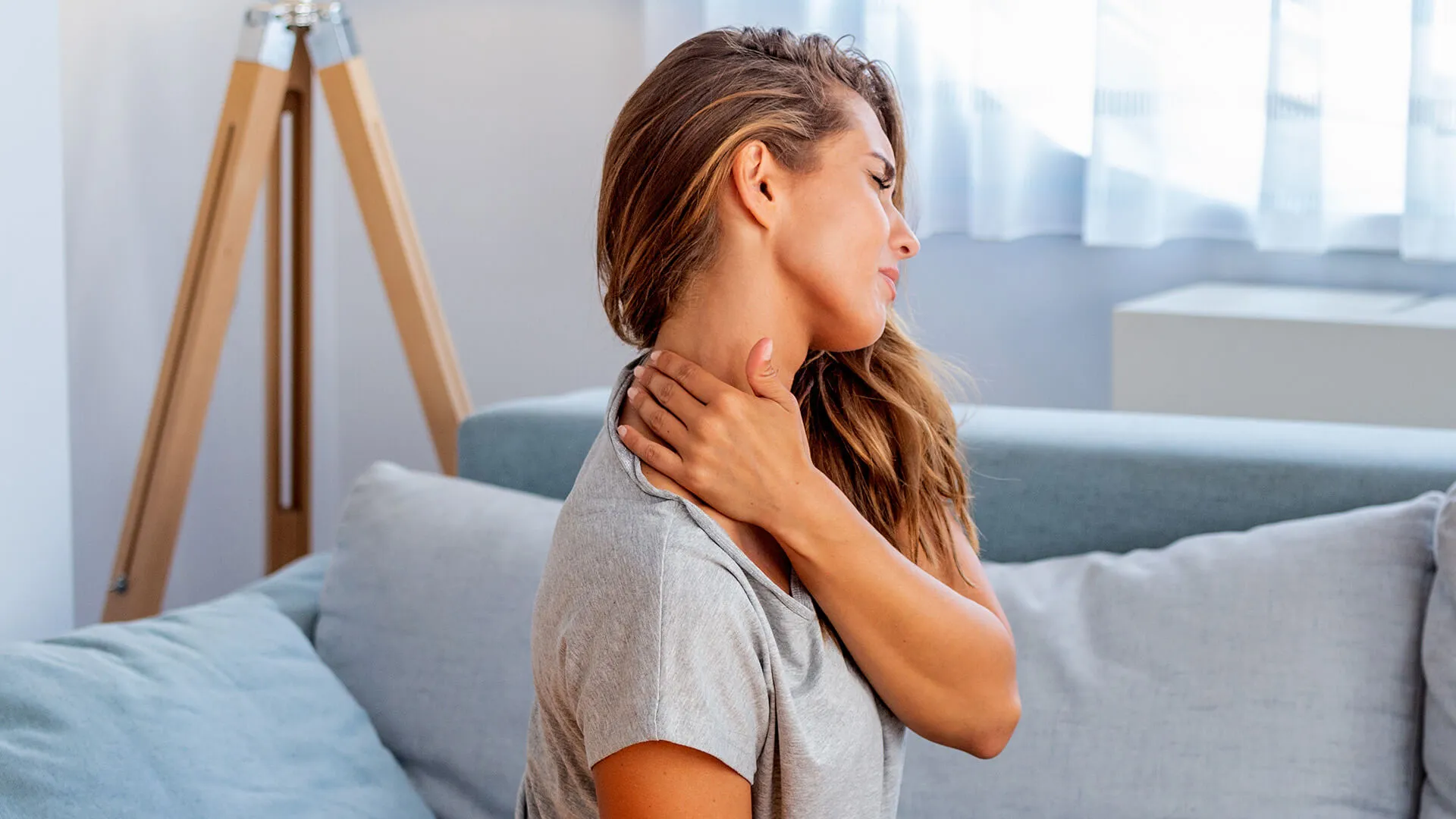 Woman holding neck in pain at home