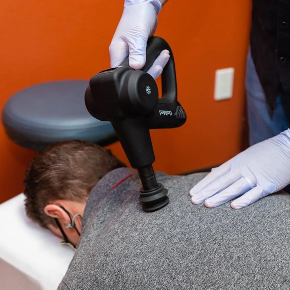 Chiropractor using massage gun on back