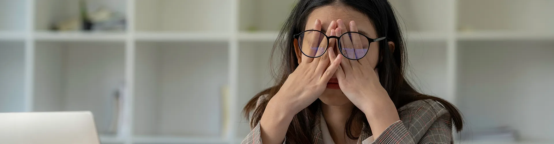 Stressed woman rubbing eyes beneath her glasses.