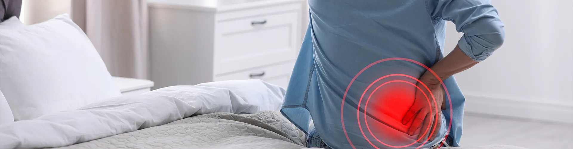 Patient seated on edge of bed holding back in discomfort.