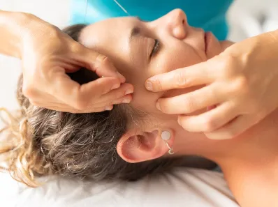 Practitioner performing facial acupuncture on patient.