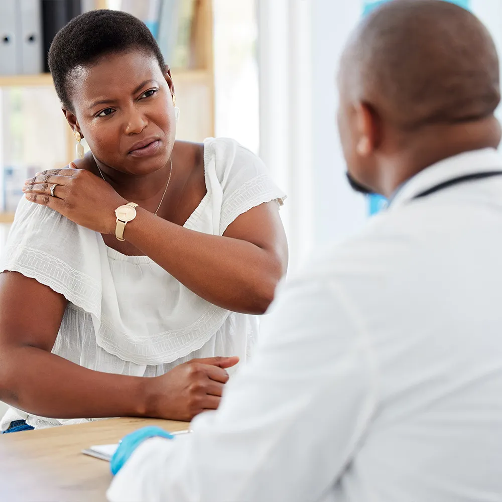Woman discussing shoulder pain with doctor.