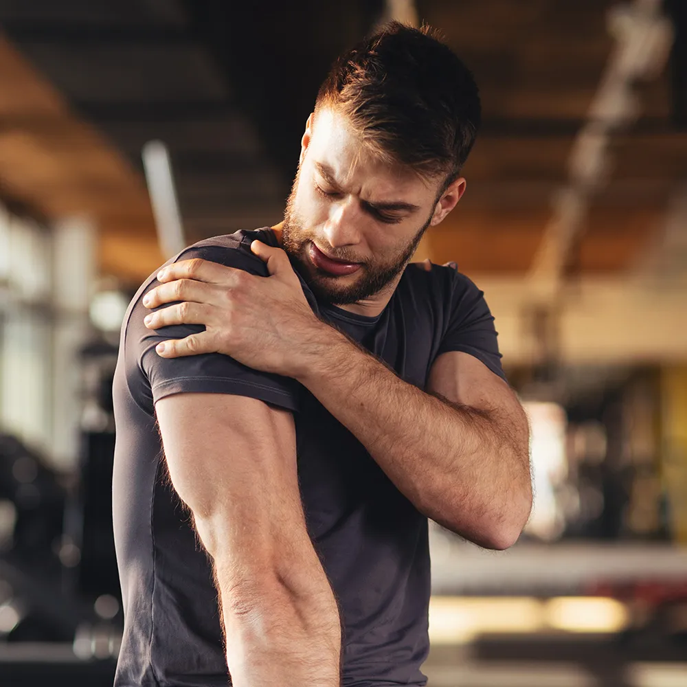 Man grimacing while holding sore shoulder.