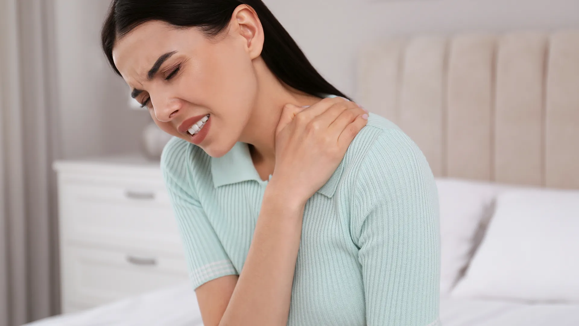 Woman holding shoulder, showing pain expression.