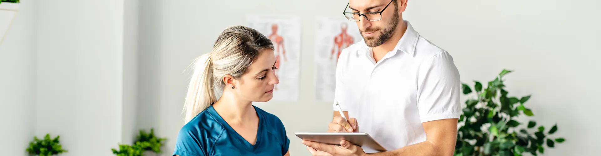 Chiropractor showing information to patient on a tablet in treatment room.