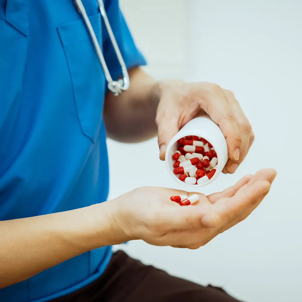 A healthcare worker pouring pills from a bottle into their hand.